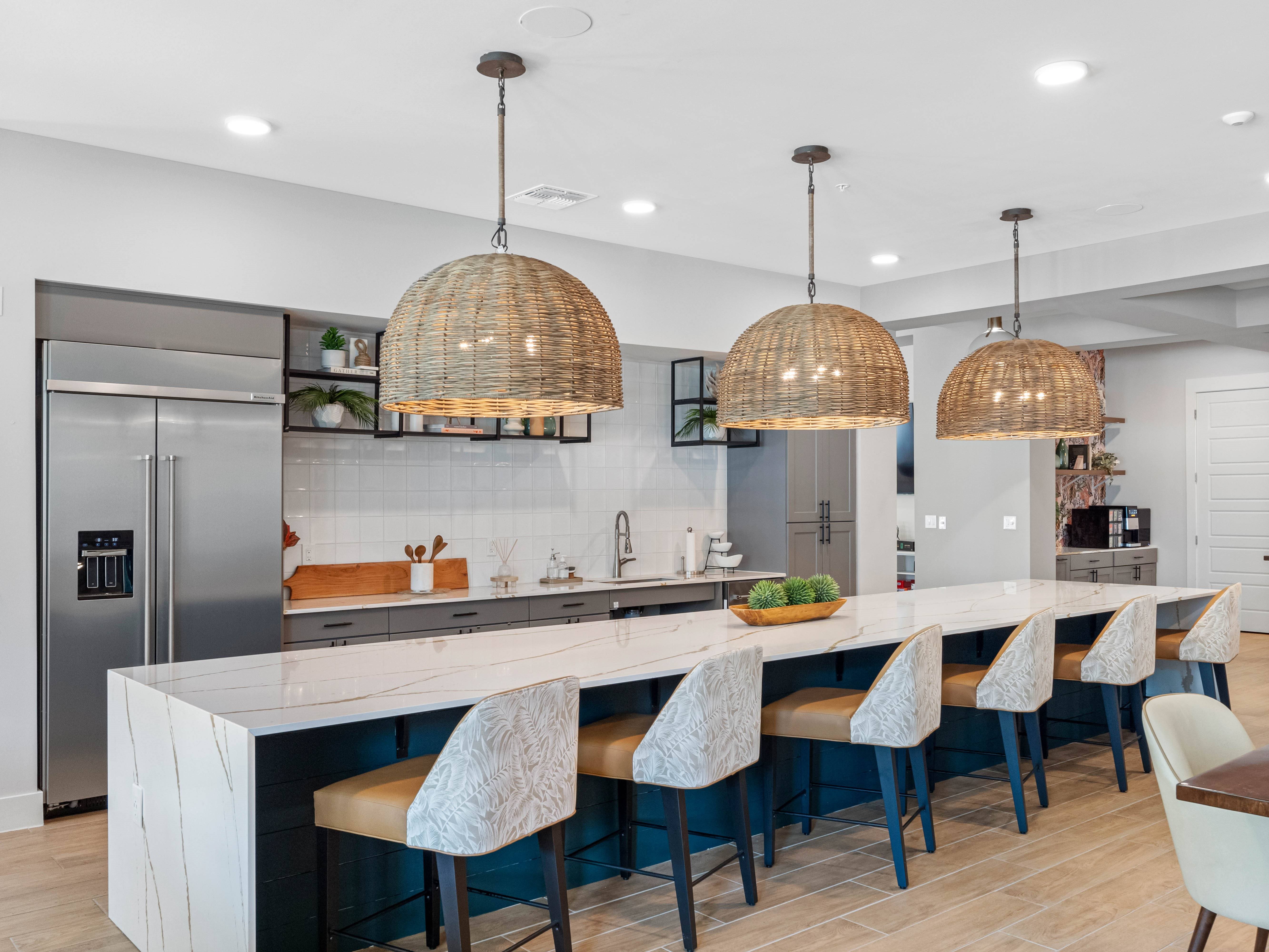 A modern kitchen with a long white island and dark blue chairs.